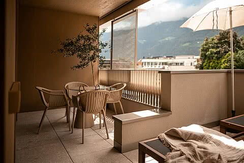 Großer Balkon im Sonnenresort Wellnesshotel in Südtirol mit Sitzbereich, Sonnenliegen, Sonnenschirm und Blick auf die Berge.