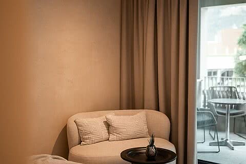 Sitzecke im Doppelzimmer des Sonnenresort Wellnesshotels in Südtirol mit Sofa, rundem Beistelltisch und Blick auf den Balkon.