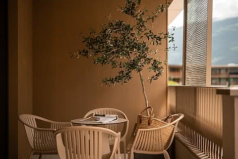 Balkon im Sonnenresort Wellnesshotel in Südtirol mit Tisch, vier Stühlen, einer Olivenpflanze und Blick auf die Berge.