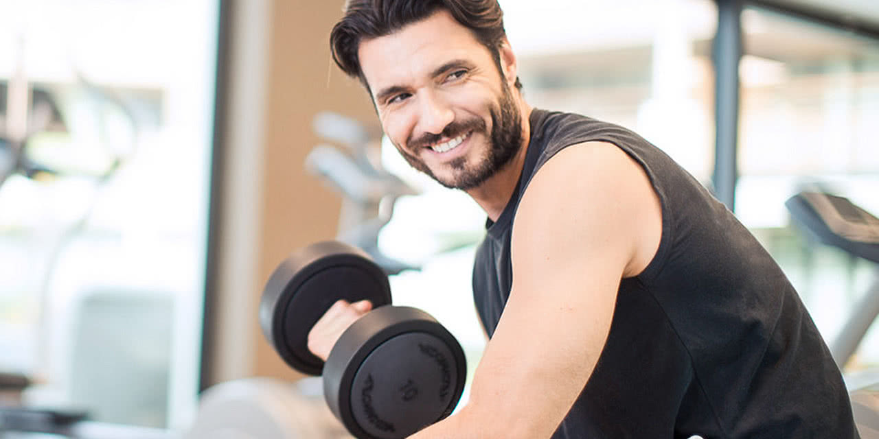 Man using dumbbells in the fitness room in the sports hotel Sonnen Resort in South Tyrol