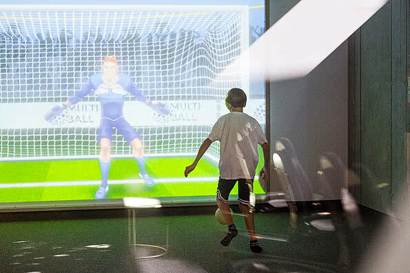 Ein Junge steht vor einer großen Projektion der iWall, während er einen Fußball vorbereitet, um zu schießen.