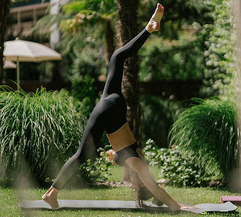Eine Frau macht im sonnigen Garten des Design Hotels Sonnen Resort Naturns Yoga.