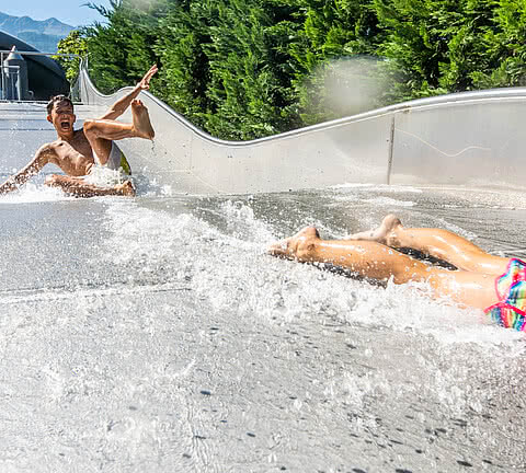 Auf der großen Wasserrutsche haben zwei Jugendliche viel Spaß, während sie durch das Wasser gleiten und die Sonne scheint.