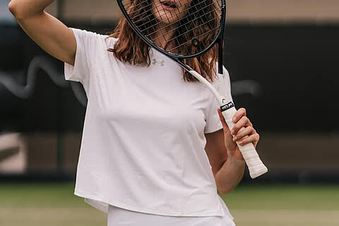 Die Tennis-Spielerin hält ihren Schläger spielerisch vor ihrem Gesicht im Design Hotel Sonnen Resort Naturns.