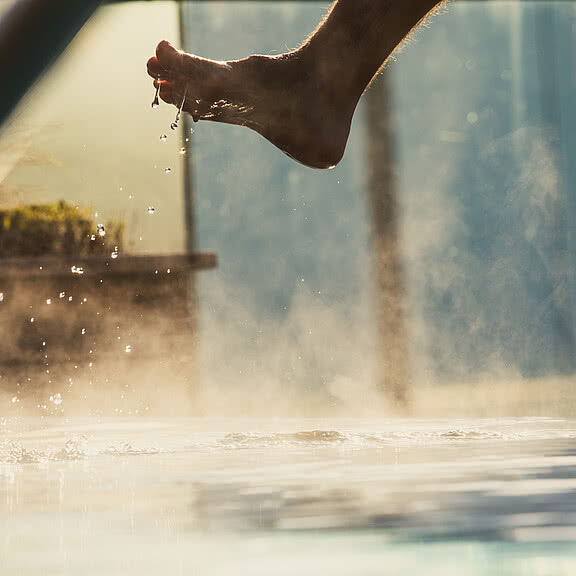 Fuß taucht in warmen Thermalwasserpool im Wellnesshotel Sonnen Resort in Südtirol ein