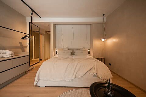Doppelzimmer im Sonnenresort Wellnesshotel in Südtirol mit großem Bett, offener Garderobe, Spiegel und dezenten Wandlampen.