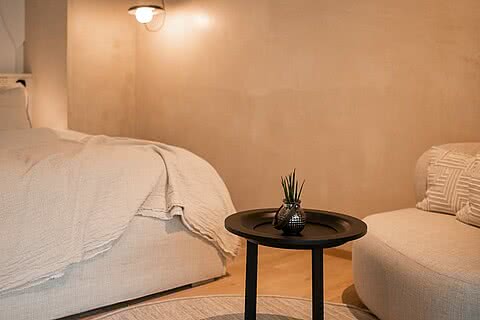 Sitzecke im Doppelzimmer des Sonnenresort Wellnesshotels in Südtirol mit rundem Beistelltisch, Sessel und Bett im Hintergrund.