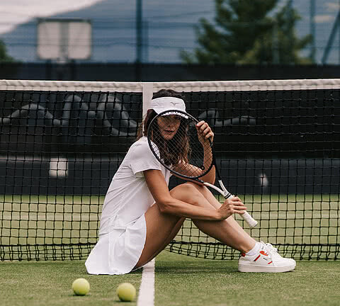 Eine Tennis-Spielerin sitzt entspannt auf dem Tennisplatz im Design Hotel Sonnen Resort Naturns.